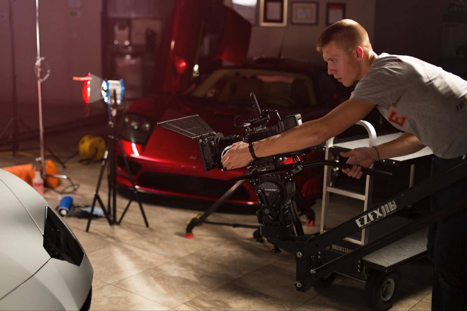 Luke operating a camera on a jib in a studio, beside a red sports car